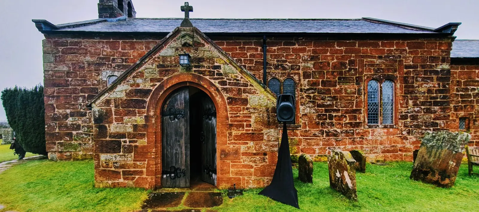 A red sandstone village church in Cumbria with gravestones in the foreground