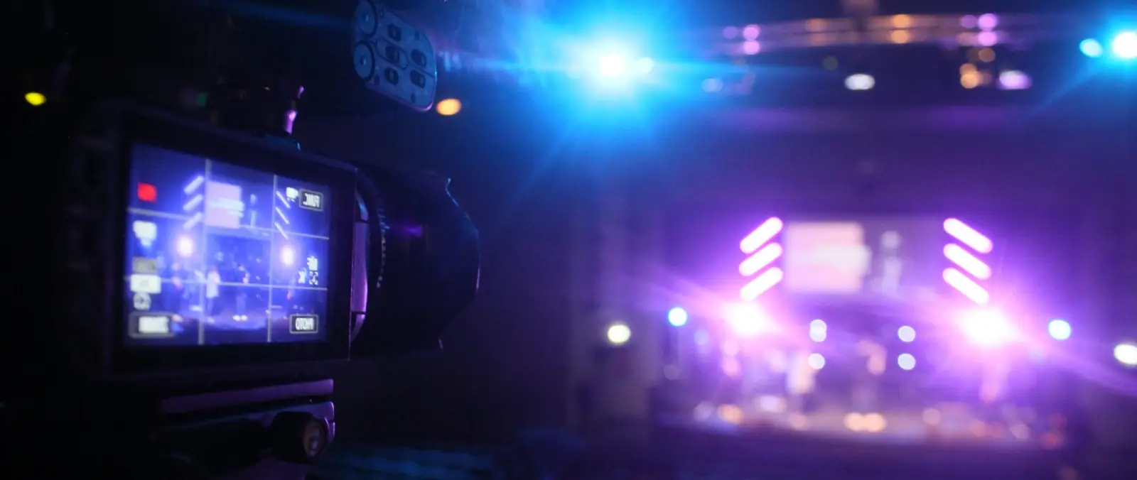A camera monitor in the foreground showing the stage, with the band lit in purple and blue behind it